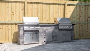 Ein Grill für den Außenbereich mit Steinunterbau und Metallschränken vor einer Holzzahlung.