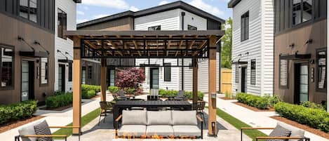 A modern outdoor patio with a pergola, seating, and a fire feature.
