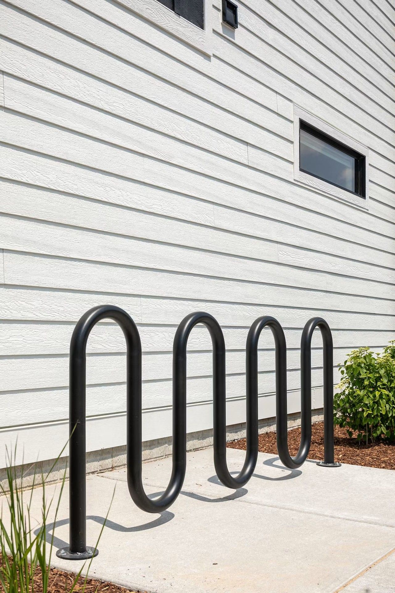 Un support à vélos en métal se trouve devant un bâtiment blanc dont le revêtement extérieur est constitué de panneaux horizontaux.