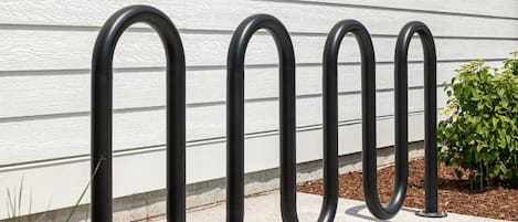 Un support à vélos en métal se trouve devant un bâtiment blanc dont le revêtement extérieur est constitué de panneaux horizontaux.