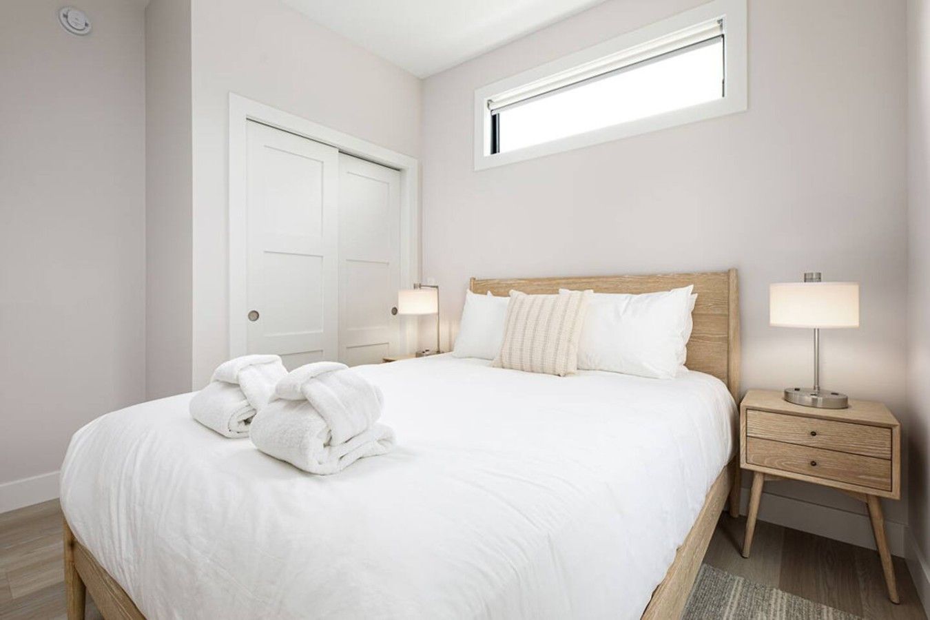 Quarto de hotel com uma cama grande, duas luminárias de cabeceira, uma cabeceira de madeira, uma janela e uma porta.