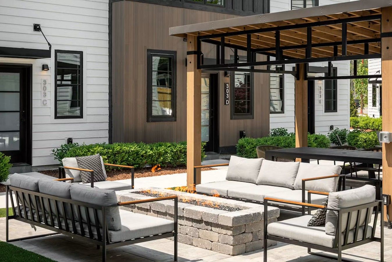 Un espace extérieur moderne aménagé avec des sièges, un foyer, une pergola et une vue sur un immeuble d’habitation.