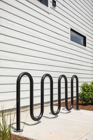 A metal bike rack in front of a white building with horizontal siding. - Hamilton Place | Sagewood Building 6BR | Near Downtown Beaches (Traverse City)
