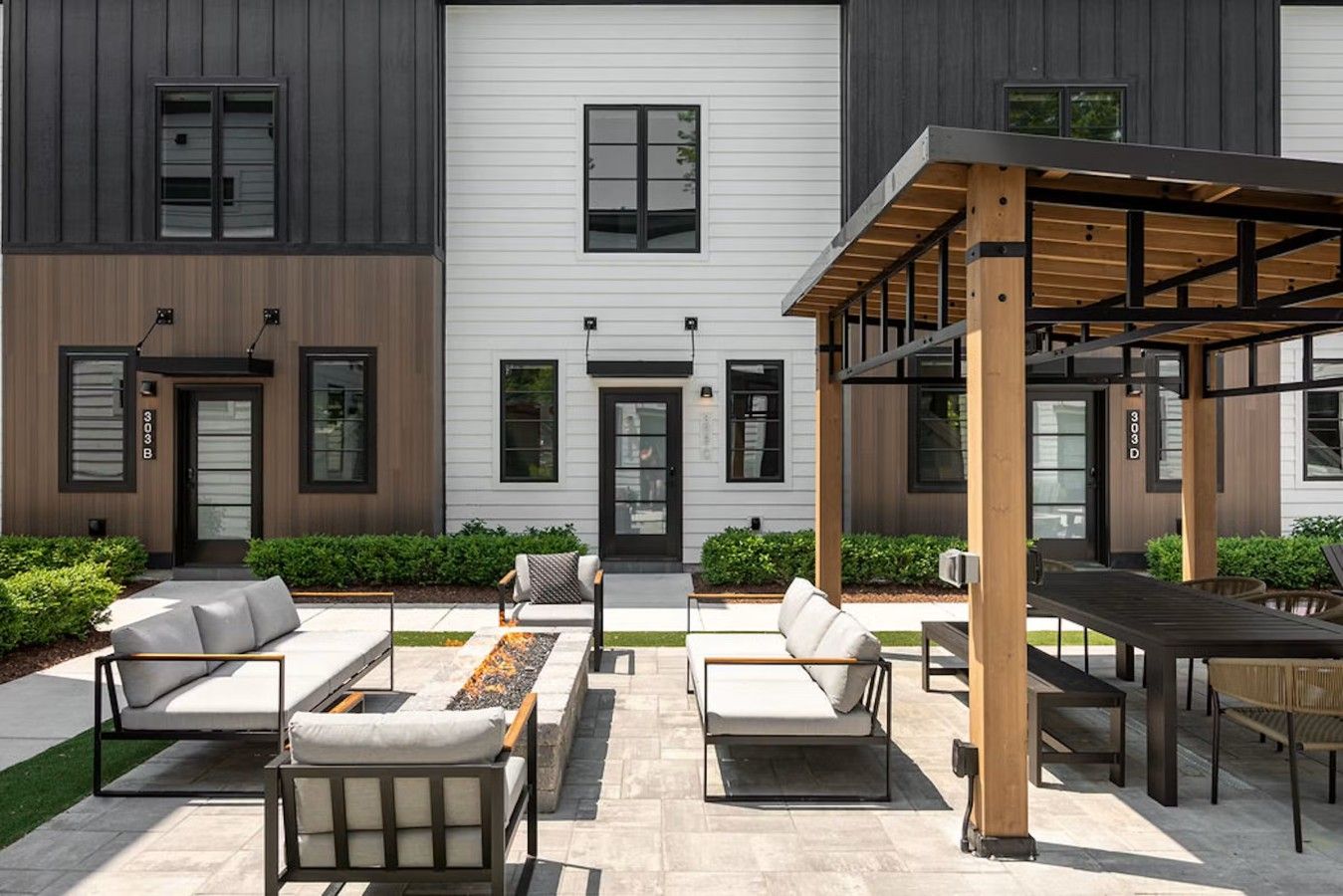 A modern two-story building with a covered outdoor seating area, a fire pit, and a well-maintained garden.