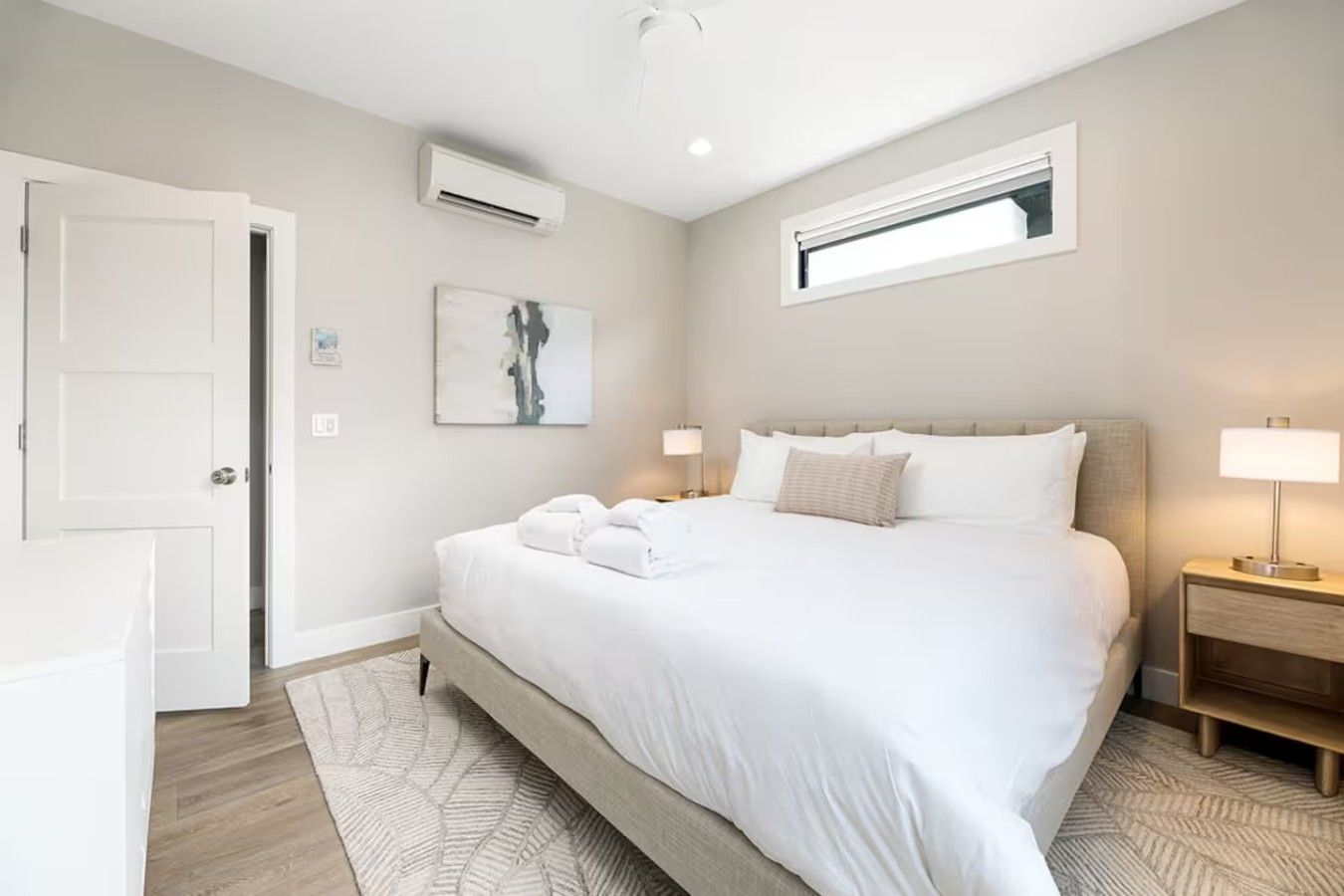 Una habitación de hotel moderna con una cama grande, dos mesitas de noche con lámparas, un ventanal y un equipo de aire acondicionado.