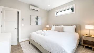 Ein modernes Hotelzimmer mit einem großen Bett, zwei Nachttischen mit Lampen, einem Fenster und einer Klimaanlage.
