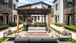 En moderne udendørs terrasse med pergola, siddepladser og bålsted.