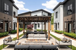 En modern uteplats med en pergola, sittplatser och en eldstad.