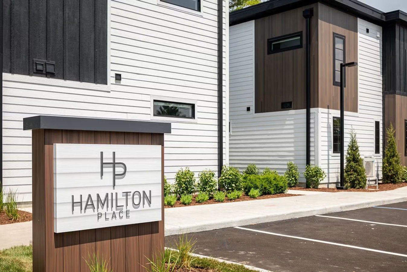 A modern building with a sign reading 'Hamilton Place' and a parking lot in front.