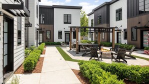 En moderne udendørs terrasse med siddepladser og bålsted, omgivet af velholdt beplantning.