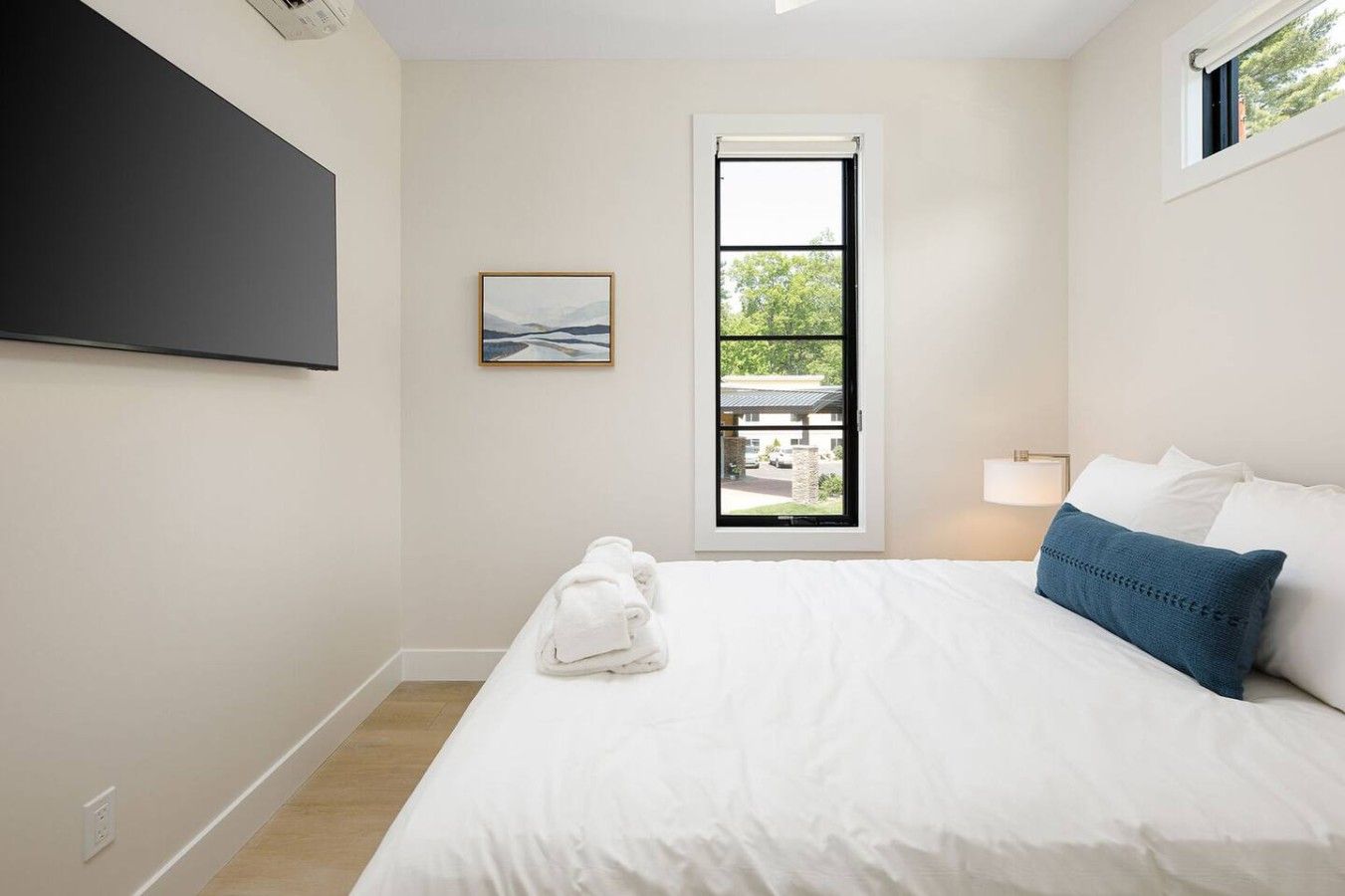 Une chambre d’hôtel avec un lit, une fenêtre donnant sur un paysage agréable, un tableau accroché au mur et une serviette sur le sol.