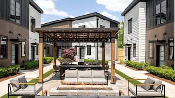 Una terrazza esterna moderna con pergolato, posti a sedere e un elemento decorativo a fuoco.