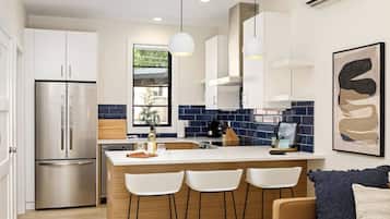 A modern kitchen with a stainless steel refrigerator, a wooden island with bar stools, and a window with a view of greenery.
