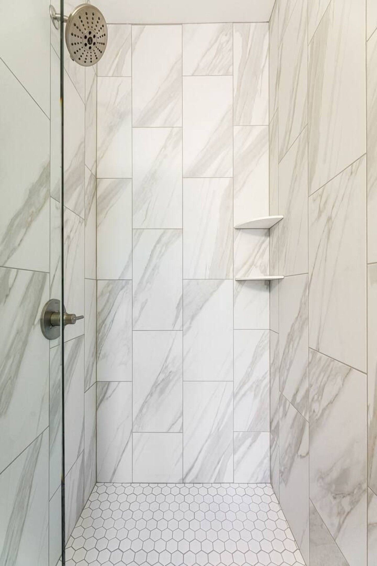Ducha con puerta de vidrio, azulejos de mármol blanco y un diseño de baldosas hexagonales en el suelo.