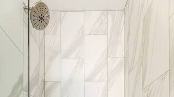 Ducha con puerta de vidrio, azulejos de mármol blanco y un diseño de baldosas hexagonales en el suelo.