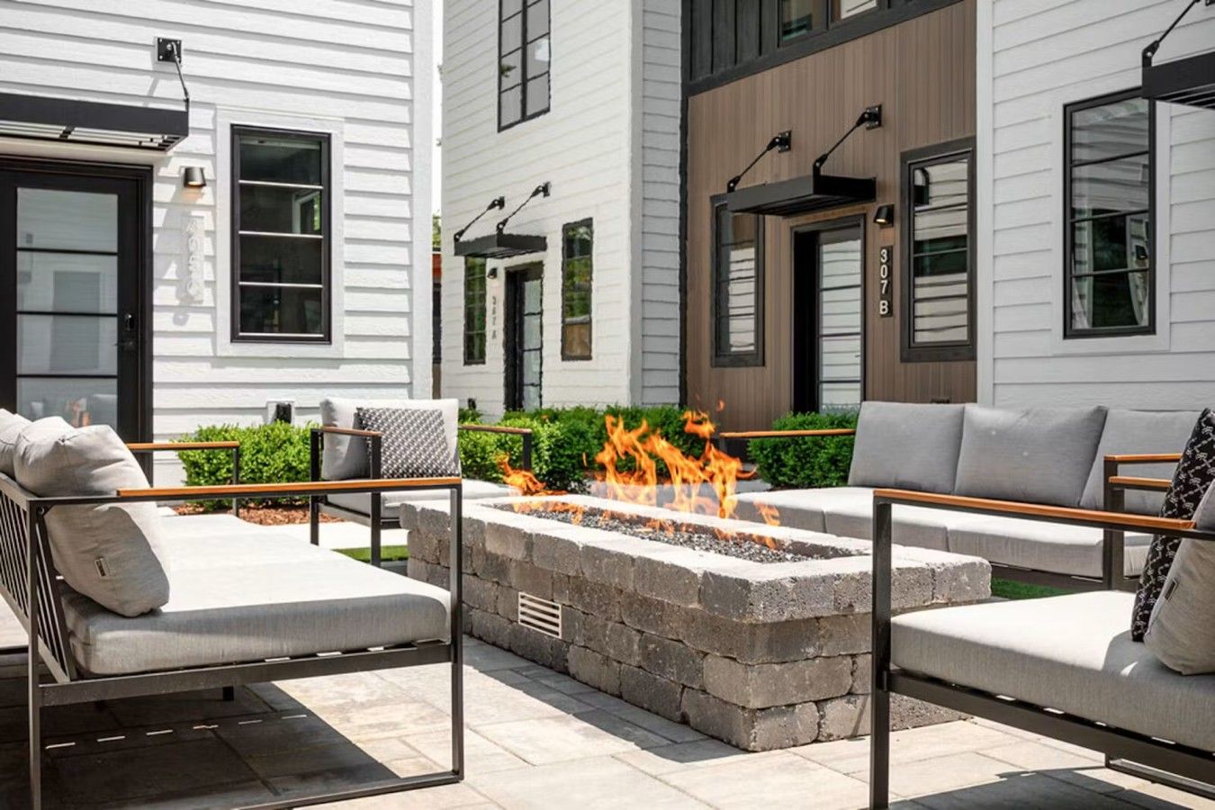 An outdoor seating area with a fire pit, surrounded by stone walls and furnished with sofas and chairs.