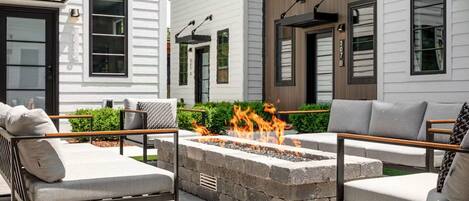 An outdoor seating area with a fire pit, surrounded by stone walls and furnished with sofas and chairs.
