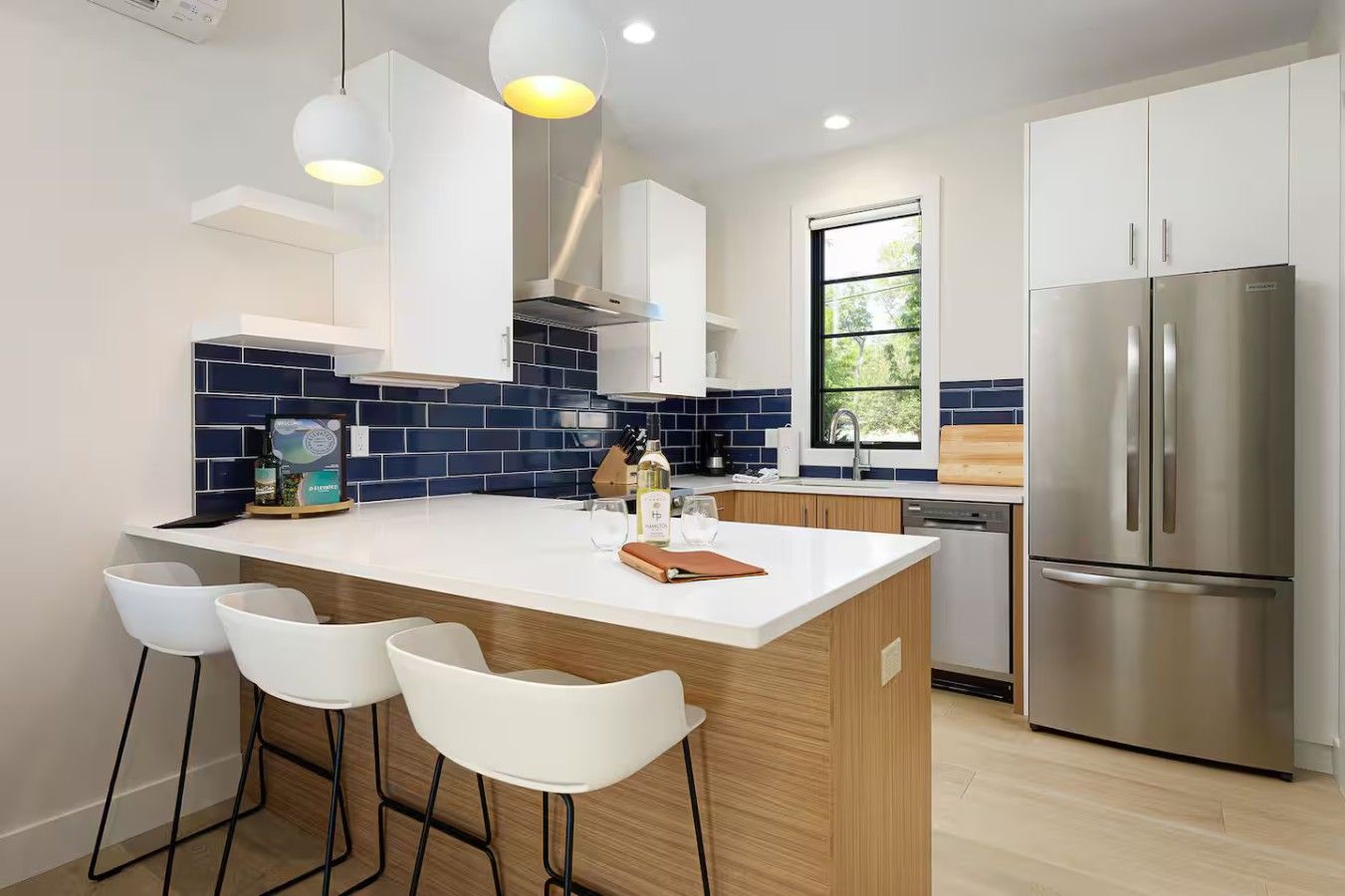 Una cocina moderna con una isla central, taburetes de bar, electrodomésticos de acero inoxidable y un ventanal que proporciona luz natural.