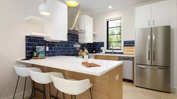 Una cocina moderna con una isla central, taburetes de bar, electrodomésticos de acero inoxidable y un ventanal que proporciona luz natural.