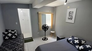Quarto com duas camas, um ventilador, um banquinho e uma porta.