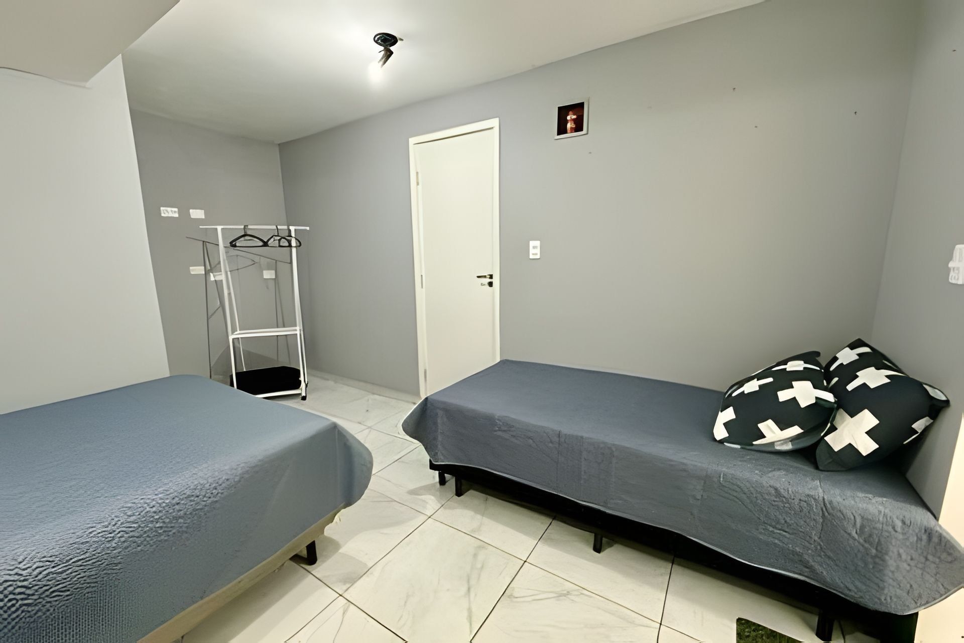 Quarto com duas camas de solteiro, um guarda-roupa e um cabideiro.