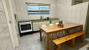 Uma cozinha com azulejos brancos, uma mesa de madeira com um banco e uma fruteira sobre a mesa.
