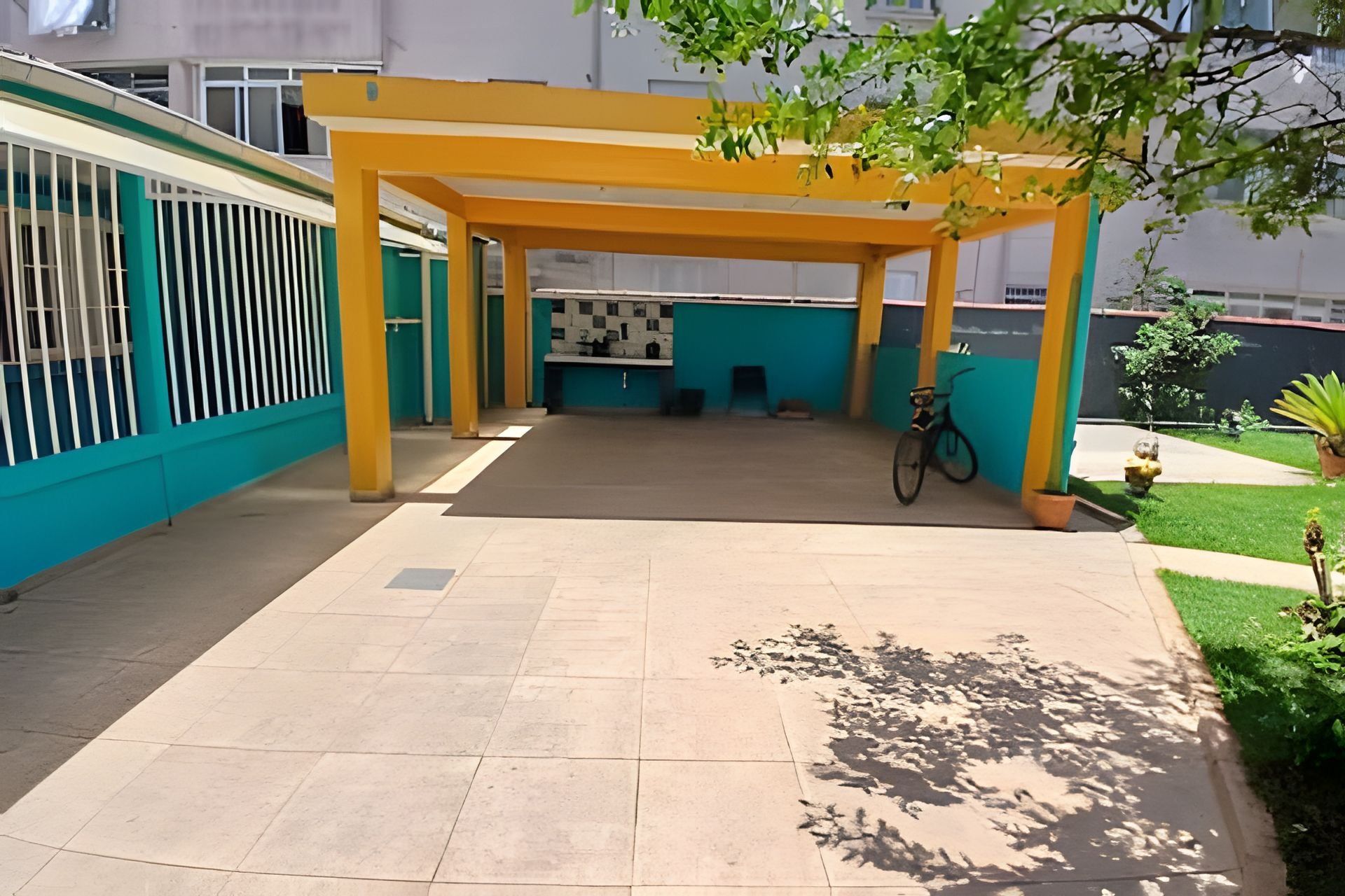 A covered outdoor area with a tiled floor, a bicycle, and a small garden with a plant and a fire hydrant.
