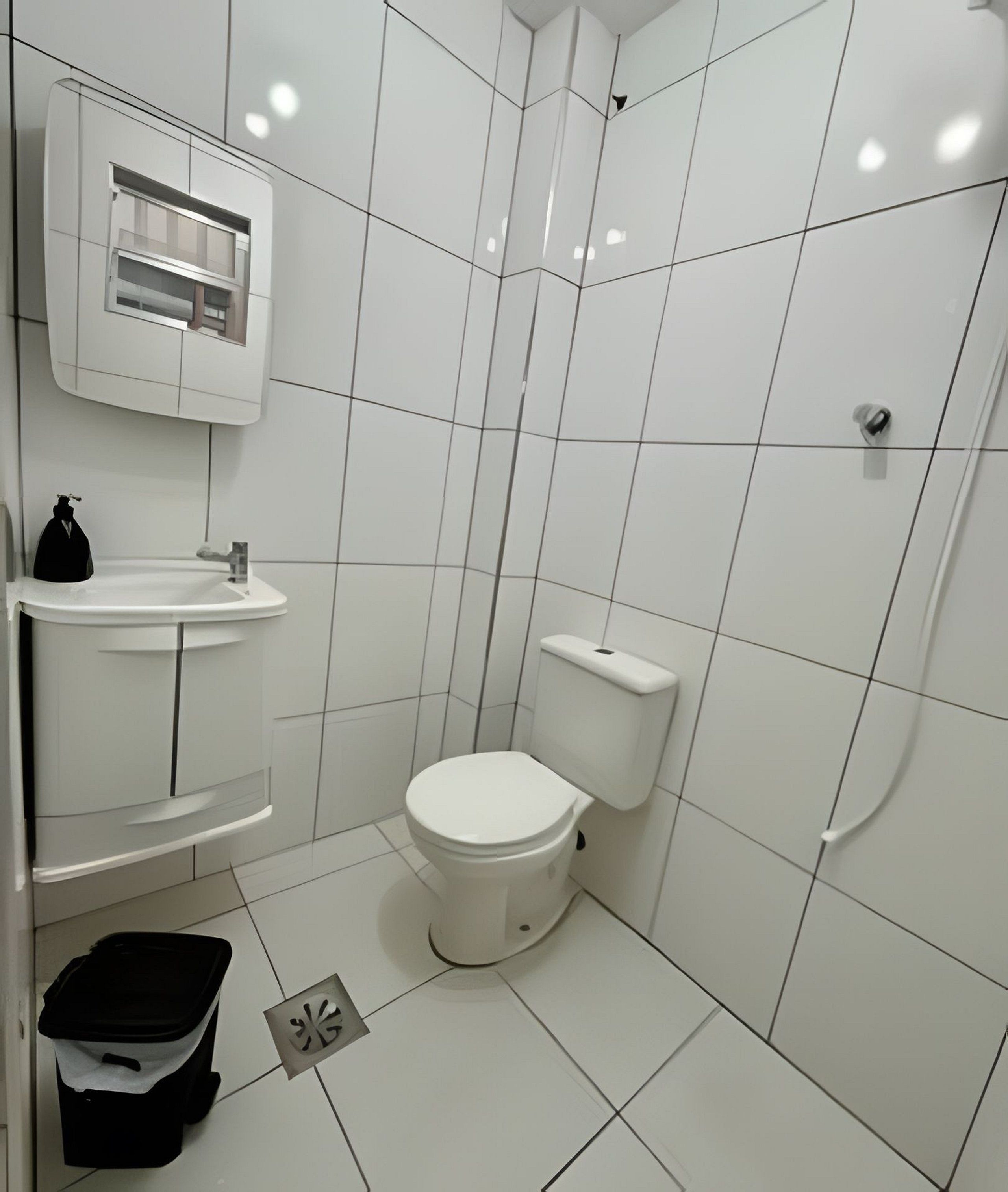 Un baño pequeño y moderno con azulejos blancos, un inodoro, un lavamanos y una ducha.