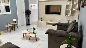 Uma sala de estar moderna com um sofá cinza, uma TV de tela plana e uma mesa de centro.