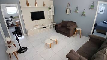 Uma sala de estar moderna com uma televisão de tela grande, um sofá marrom, duas mesinhas redondas e um móvel de entretenimento branco com objetos decorativos.