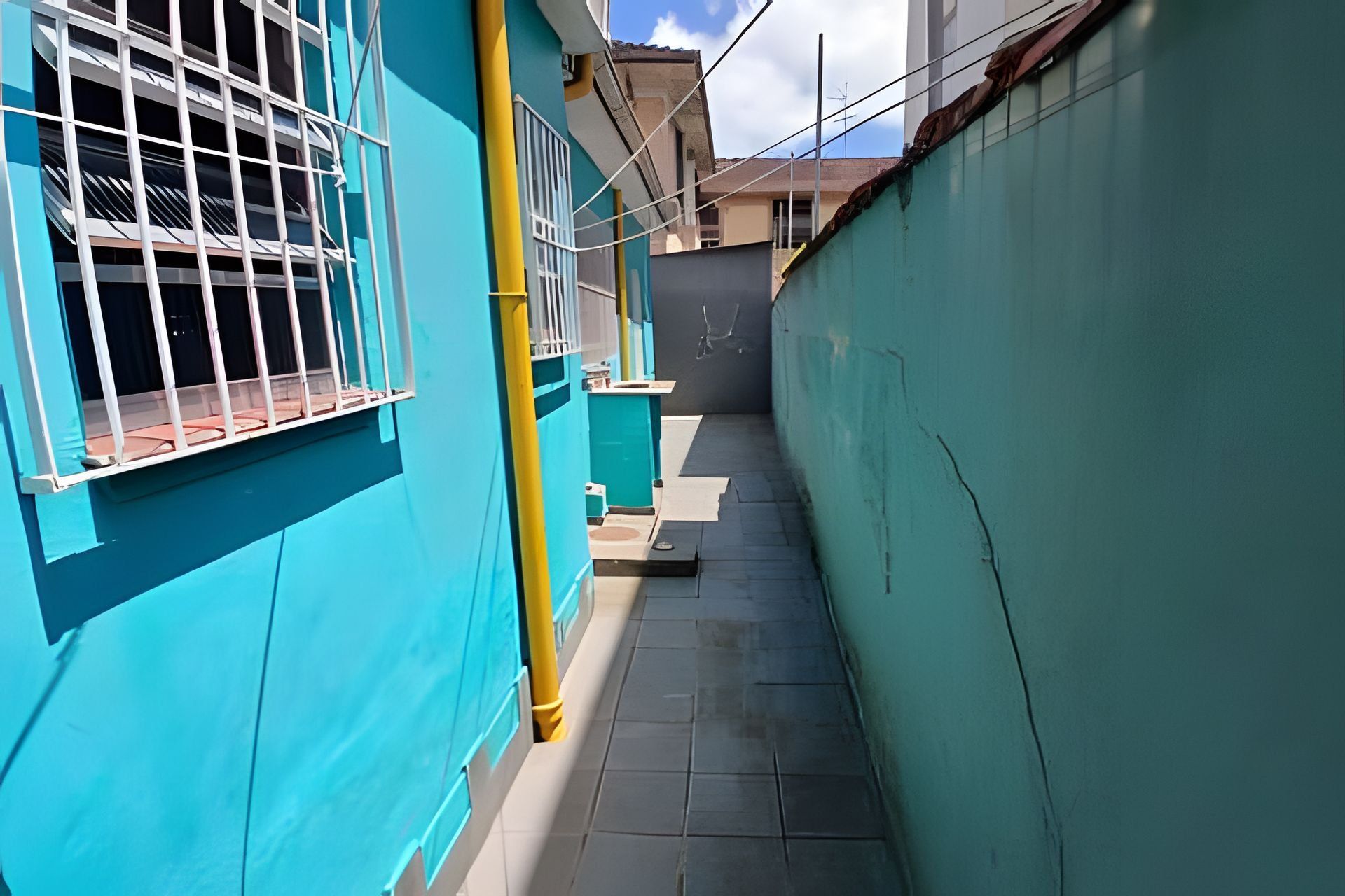 A narrow alleyway with a blue building on one side and a grey building on the other.