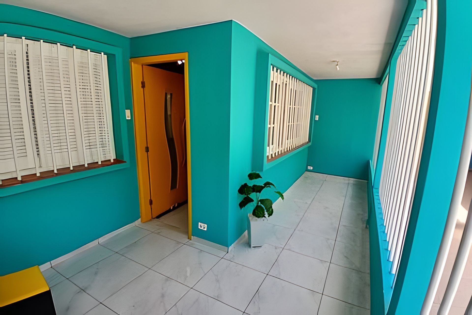 Un pasillo con paredes color verde azulado, suelo de baldosas blancas y una puerta de madera.
