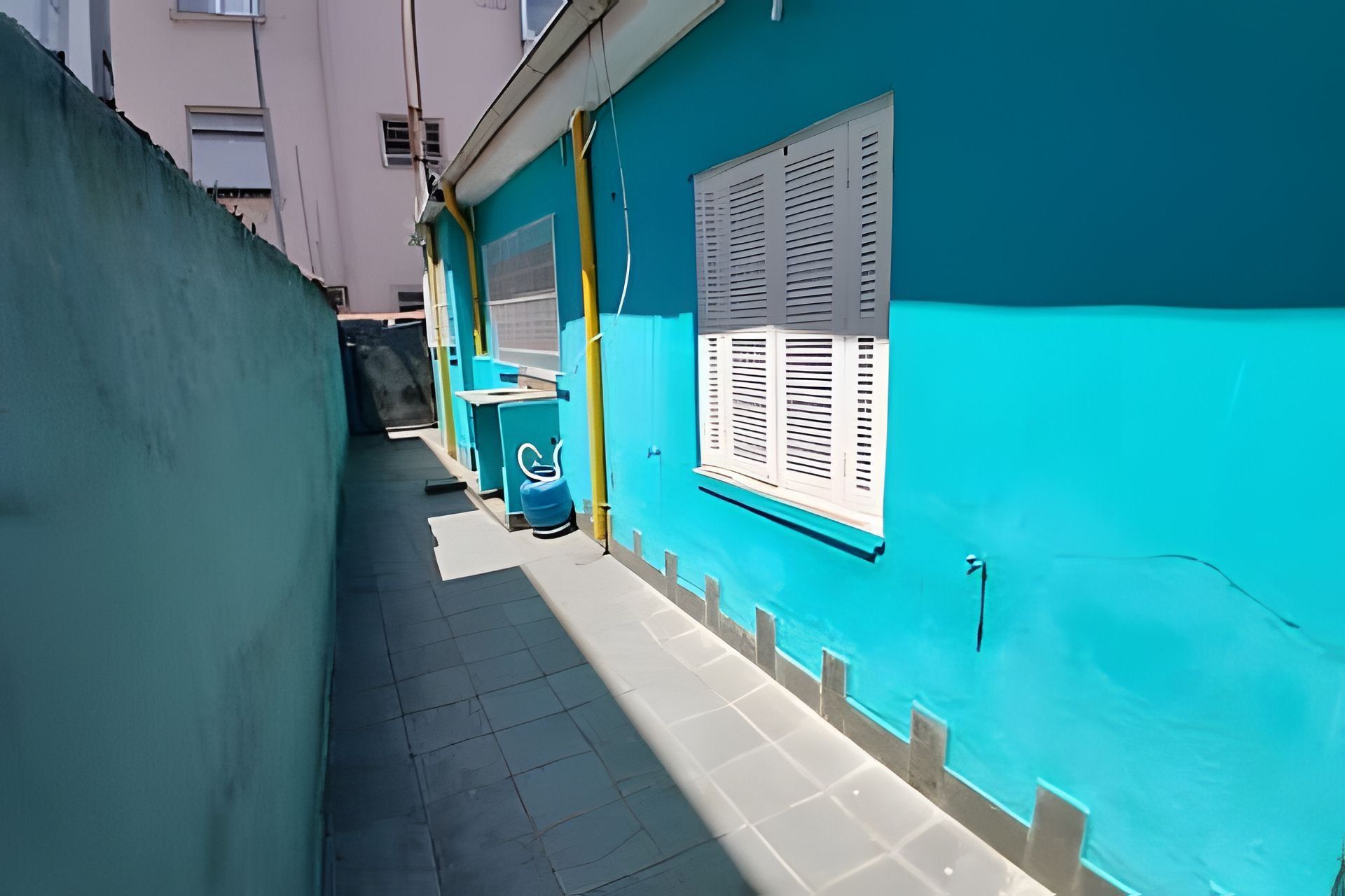 A narrow alleyway with a turquoise wall, a window with shutters, and a blue gas cylinder.