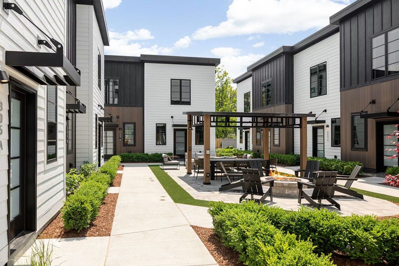 A modern outdoor patio area with seating and a fire pit, surrounded by well-maintained landscaping.