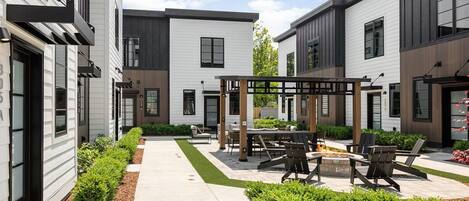 A modern outdoor patio area with seating and a fire pit, surrounded by well-maintained landscaping.