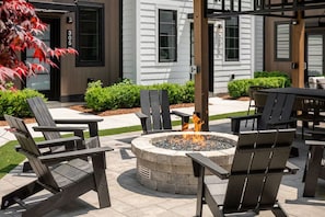 An outdoor seating area with Adirondack chairs and a stone fire pit. - Hamilton Place | Bayside Building 8BR | Near Downtown Beaches (Traverse City)