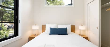 Une chambre d’hôtel avec un lit, deux tables de chevet, une fenêtre et une porte.