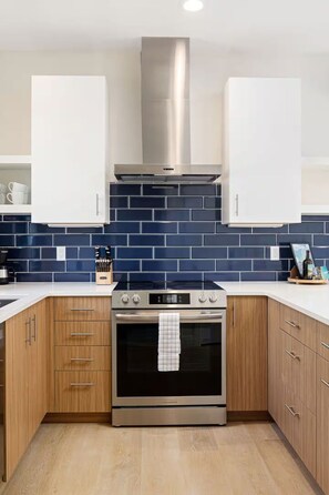 A modern kitchen with wooden cabinets, a stainless steel range hood, and a tiled backsplash. - Hamilton Place | Bayside Building 8BR | Near Downtown Beaches (Traverse City)
