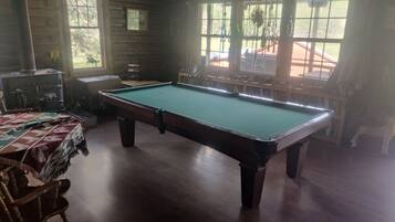 A pool table in a room with wooden walls, a window, and a view of the outdoors.