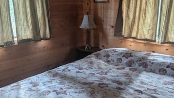 A wooden room with a bed, curtains, a lamp, and a framed picture on the wall.