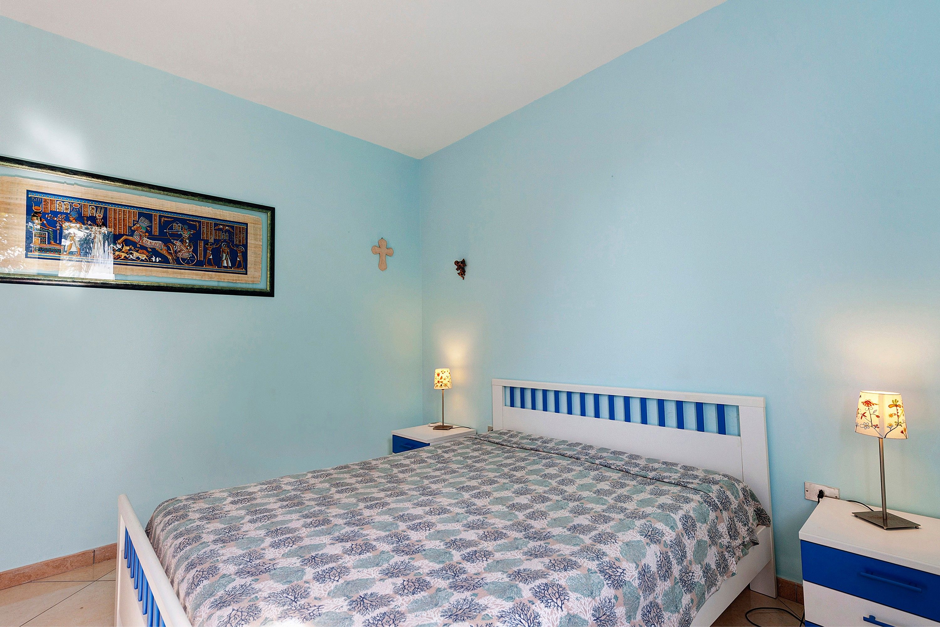 Una camera da letto con un letto, due comodini, una lampada da parete e un quadro incorniciato.