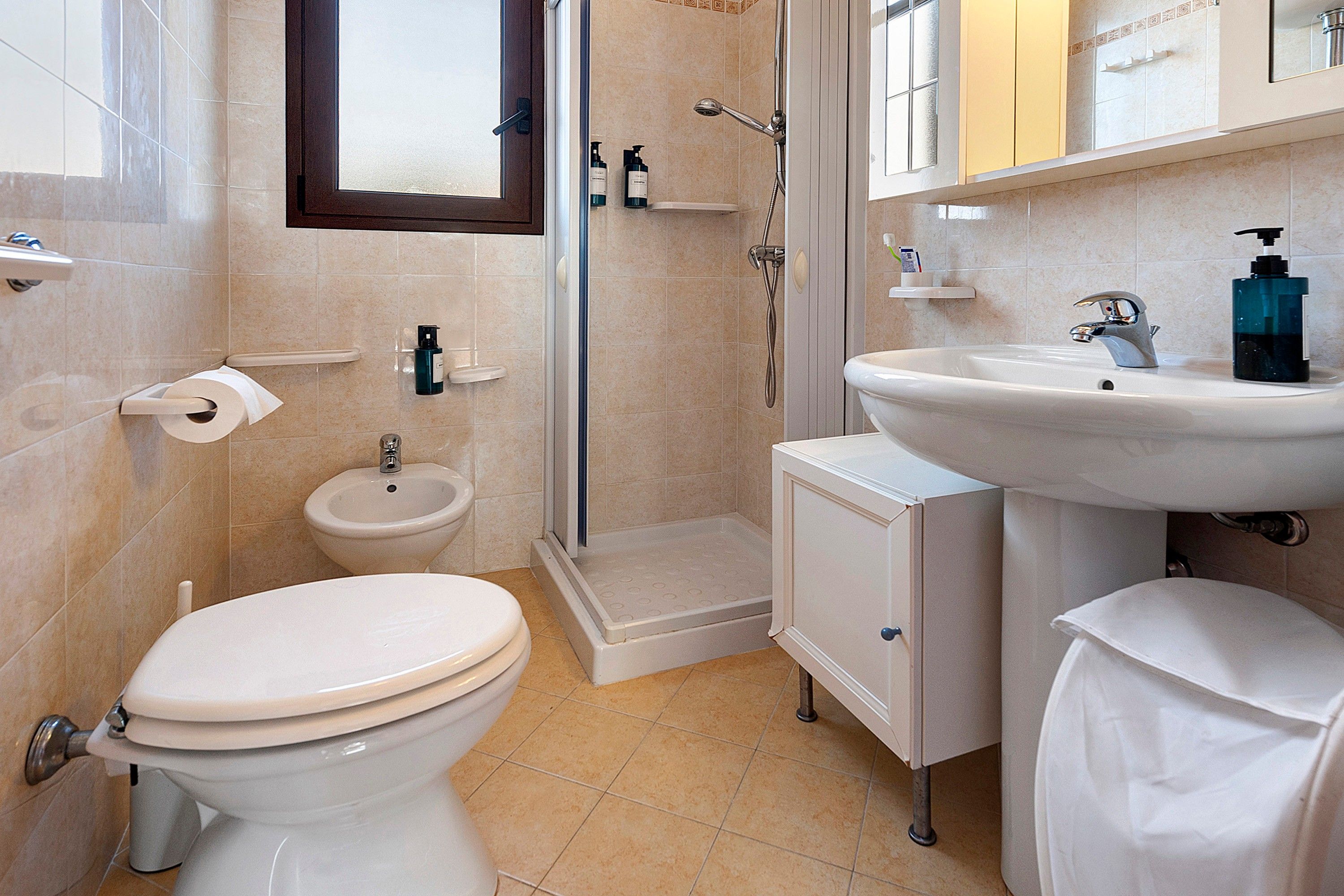 A bathroom with a toilet, bidet, shower, and sink.