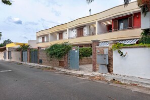 A two-story residential building with a balcony, a gated entrance, and a brick wall.