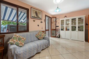 Una sala de estar con un sofá, cojines estampados, un cuadro enmarcado en la pared y un mueble con puertas de vidrio.