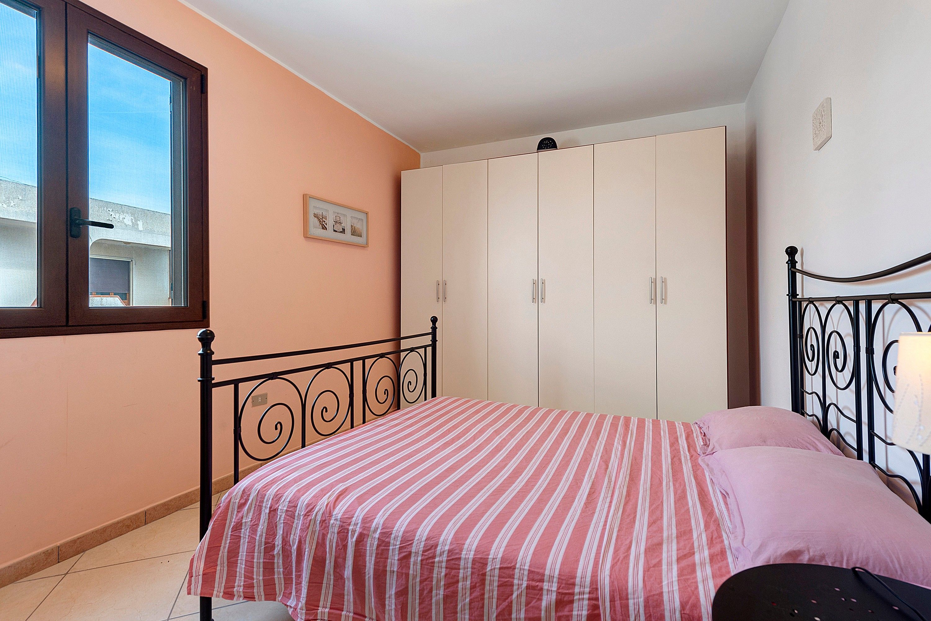 Un dormitorio con cama, armario, ventana y un cuadro colgado en la pared.