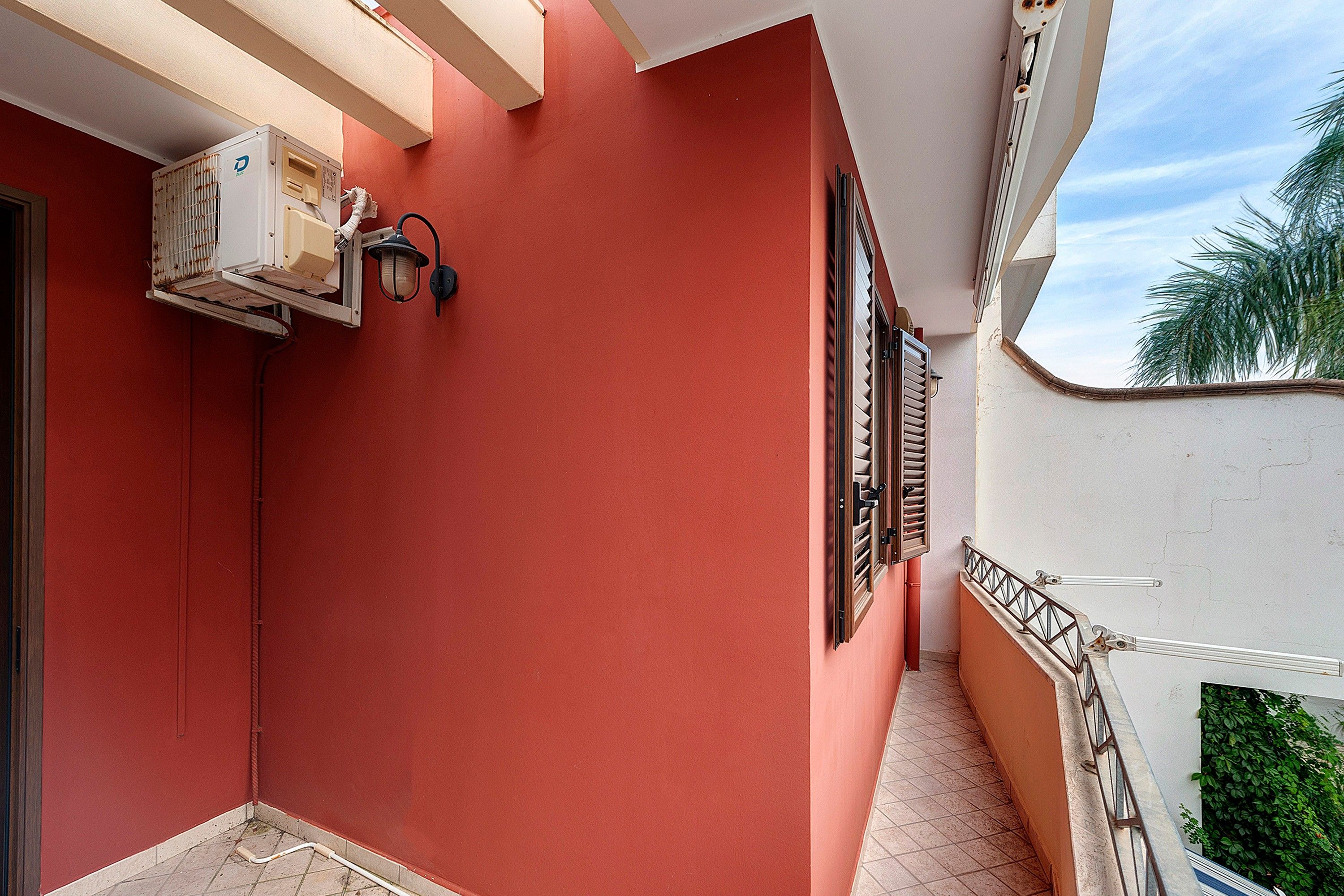 Pared exterior roja con una ventana, una puerta y un pequeño balcón con barandilla.