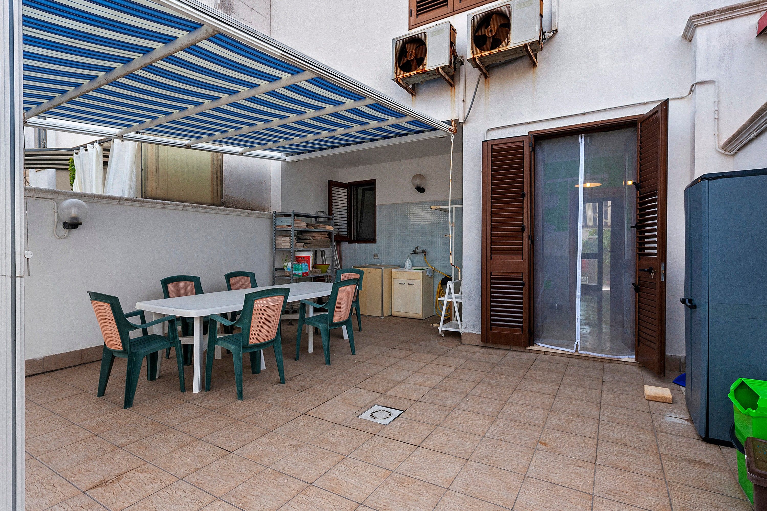 Un espace extérieur abrité, aménagé pour les repas, avec une table et des chaises, un distributeur d’eau et un petit coin cuisine équipé d’un évier et de placards.