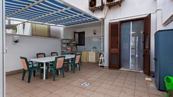 Un espace extérieur abrité, aménagé pour les repas, avec une table et des chaises, un distributeur d’eau et un petit coin cuisine équipé d’un évier et de placards.