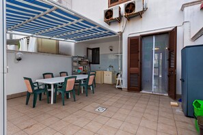 A covered outdoor dining area with a table and chairs, a water dispenser, and a small kitchen area with a sink and cabinets.