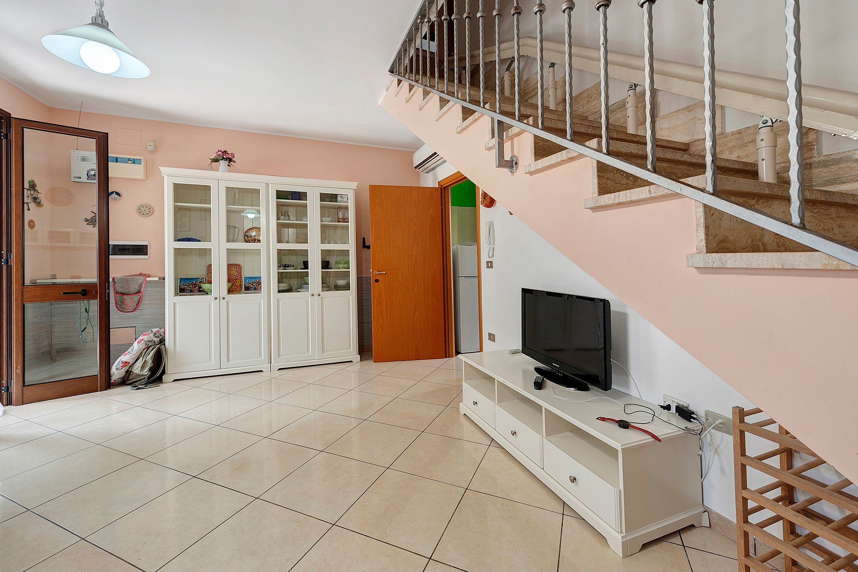 A living room with a TV, cabinets, a staircase, and a door leading to another room.